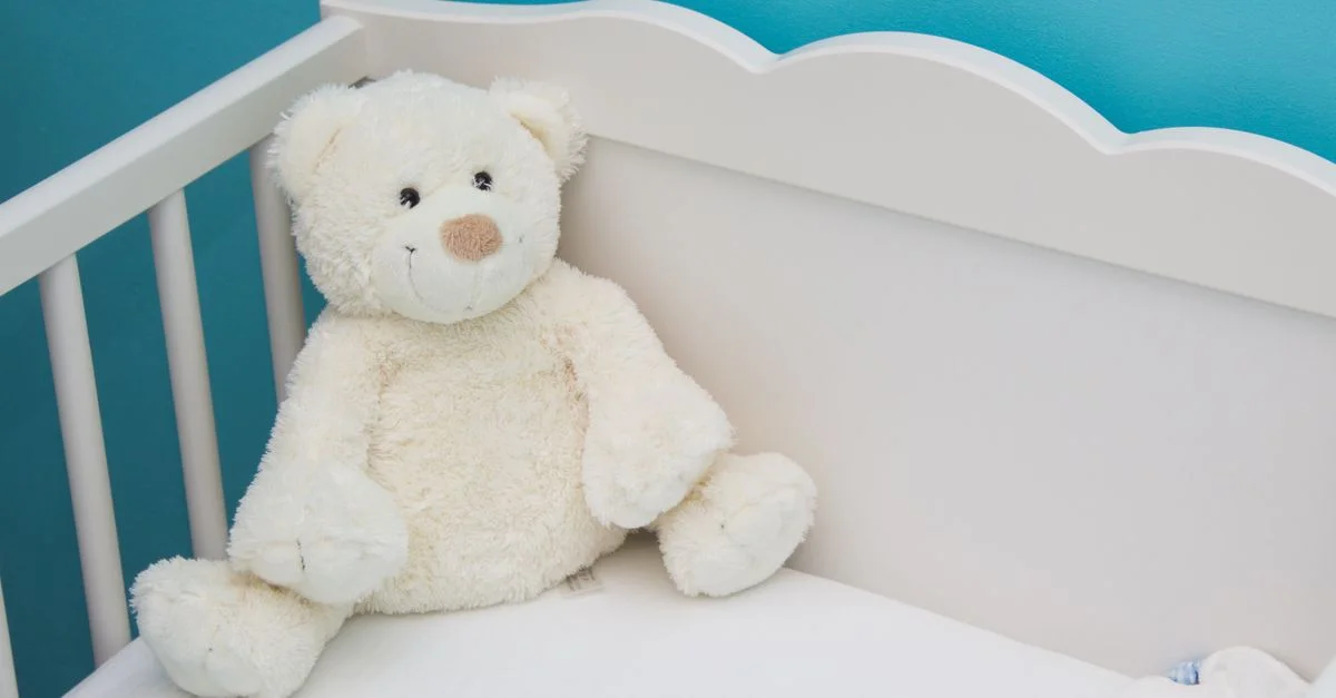 Suave oso de peluche en una cuna blanca contra una pared azul vibrante, creando una atmósfera reconfortante en la habitación del bebé.