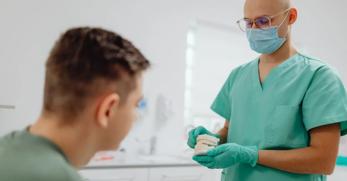 Dentiste en blouse expliquant une procédure dentaire à un patient dans un cadre de bureau.