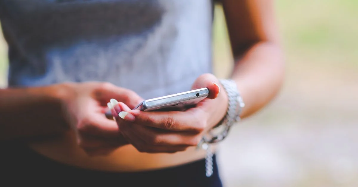 Gros plan d'une femme textant sur un smartphone à l'extérieur, mettant en avant la connectivité mobile et la technologie.