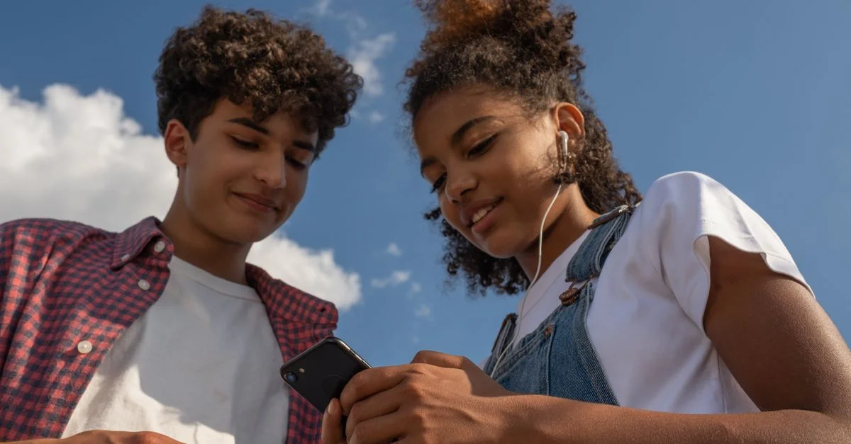 Deux adolescents écoutent de la musique ensemble en extérieur avec un smartphone et des écouteurs.