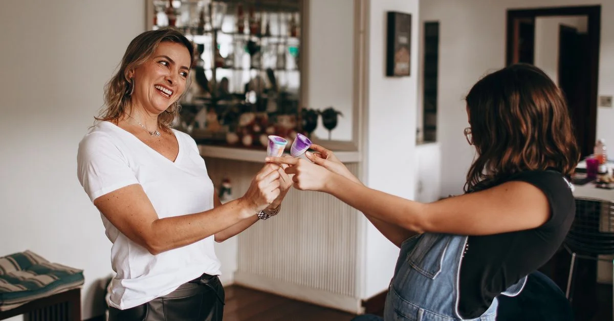 Una madre y una hija alegres chocan copas en un acogedor ambiente de sala de estar. Captura la unión familiar.