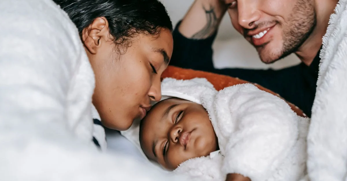 Madre y padre abrazan a su bebé dormido en una escena acogedora y amorosa.