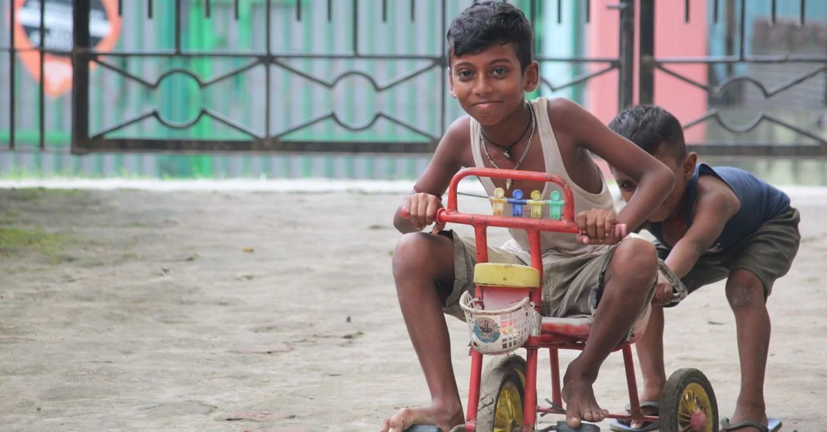 Deux enfants s'amusent à conduire un tricycle vintage à l'extérieur, capturant l'essence d'une enfance joyeuse.
