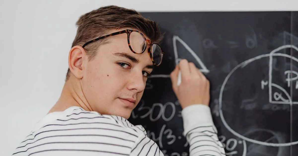 Chico adolescente escribiendo ecuaciones matemáticas en una pizarra en un aula.