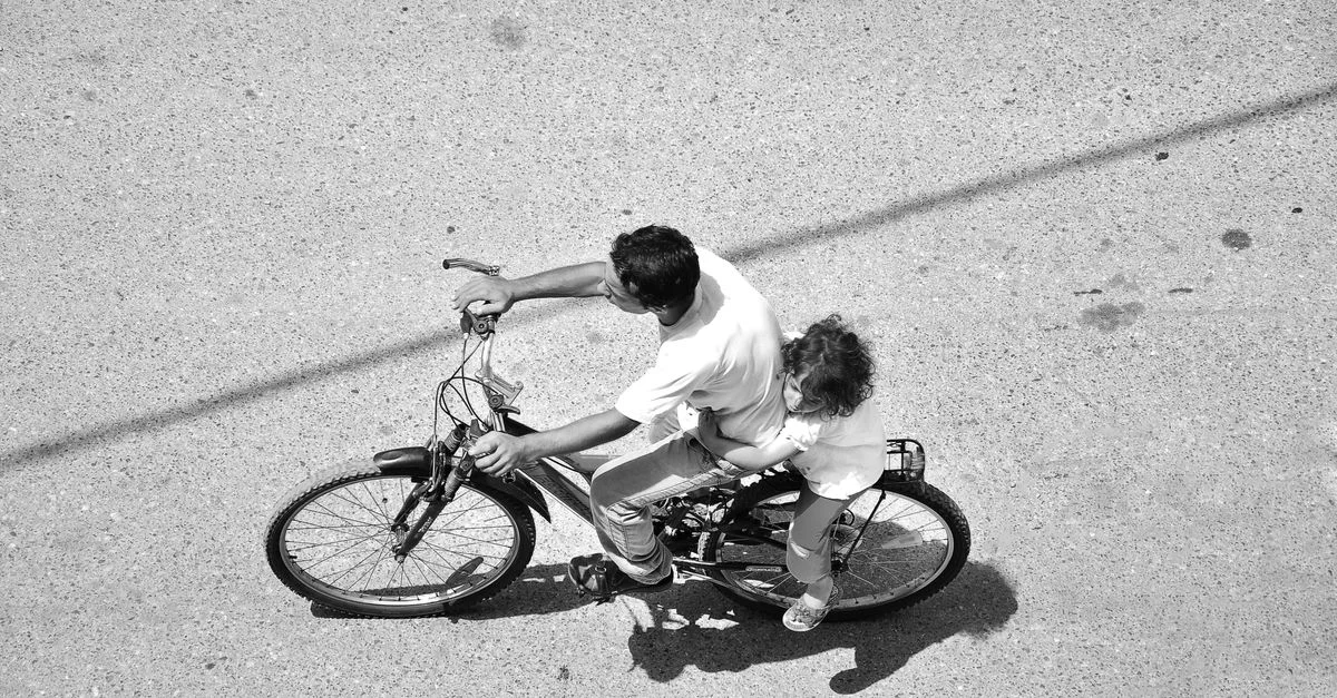 Una foto en blanco y negro de un padre y un hijo montando en bicicleta vista desde arriba.