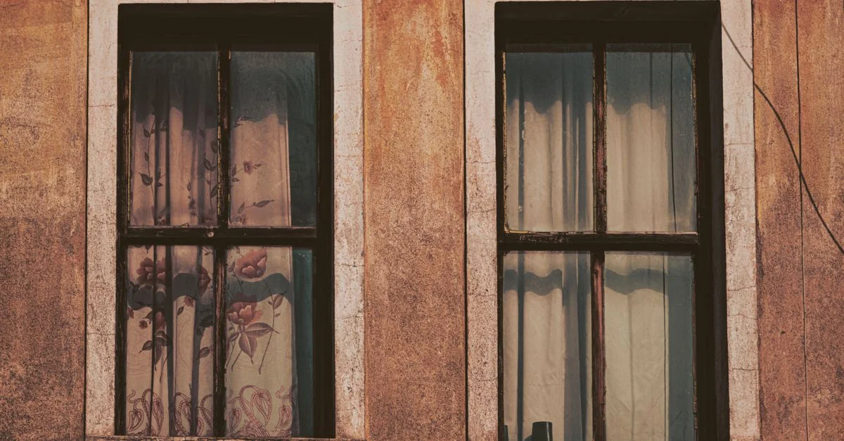 Vista cercana de una ventana doble rústica con cortinas florales, exhibiendo una elegancia envejecida.