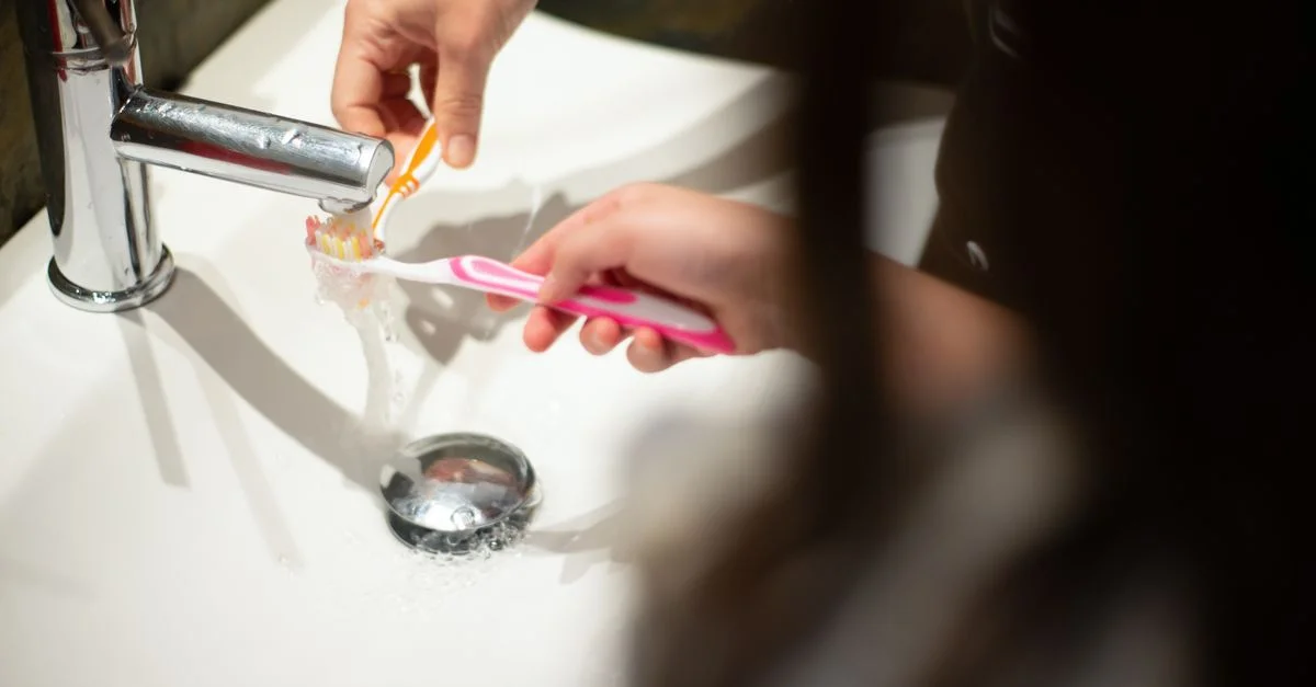 Gros plan d'un enfant se brossant les dents au lavabo sous l'eau courante.