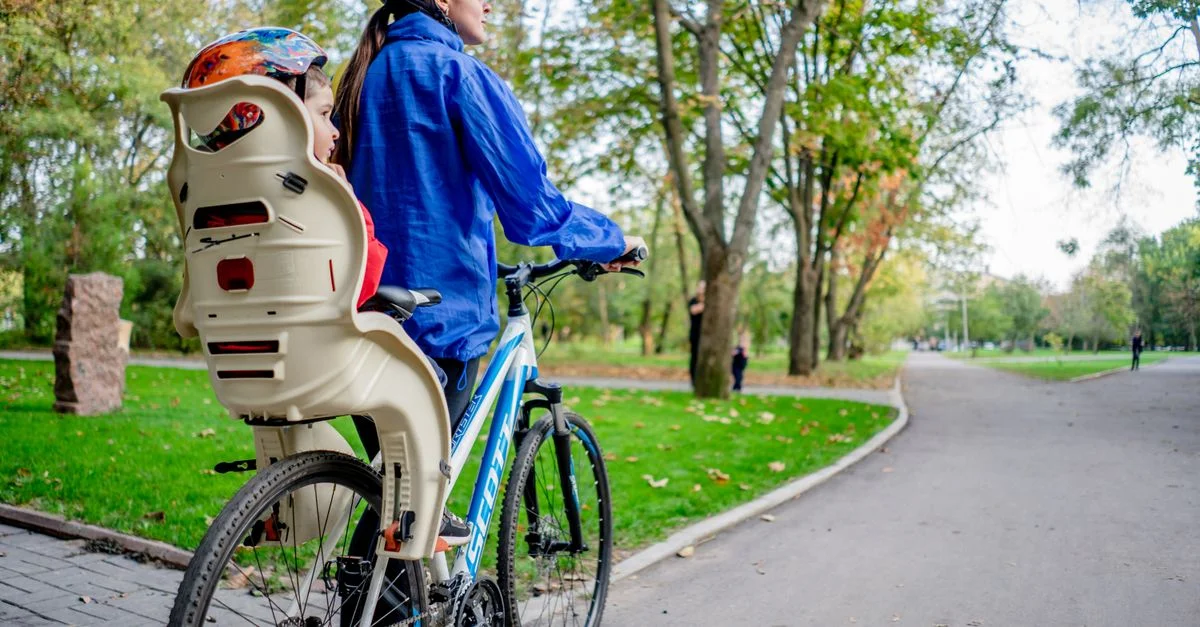 Una mujer monta en bicicleta con un asiento para niño al aire libre en un parque vibrante.