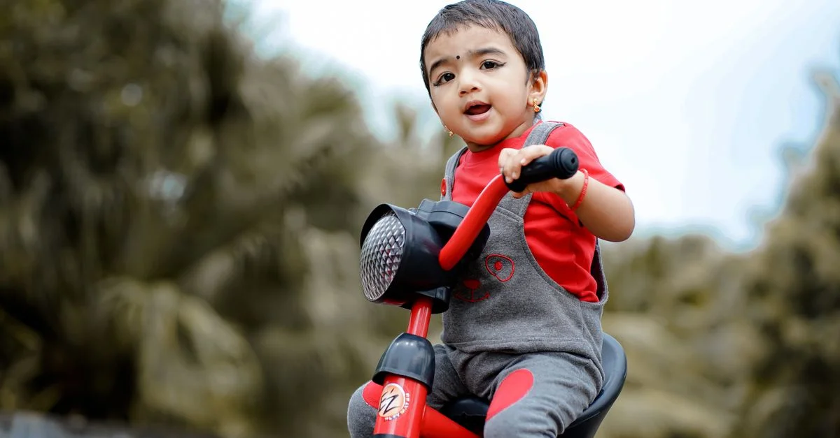 Enfant mignon profitant d'une balade sur un tricycle dans un cadre extérieur verdoyant, mettant en avant la joie et l'innocence.