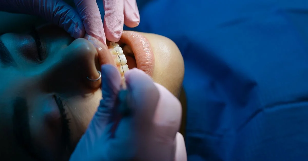 Un dentiste examine les dents d'un patient lors d'une procédure dentaire sous des lumières cliniques vives.