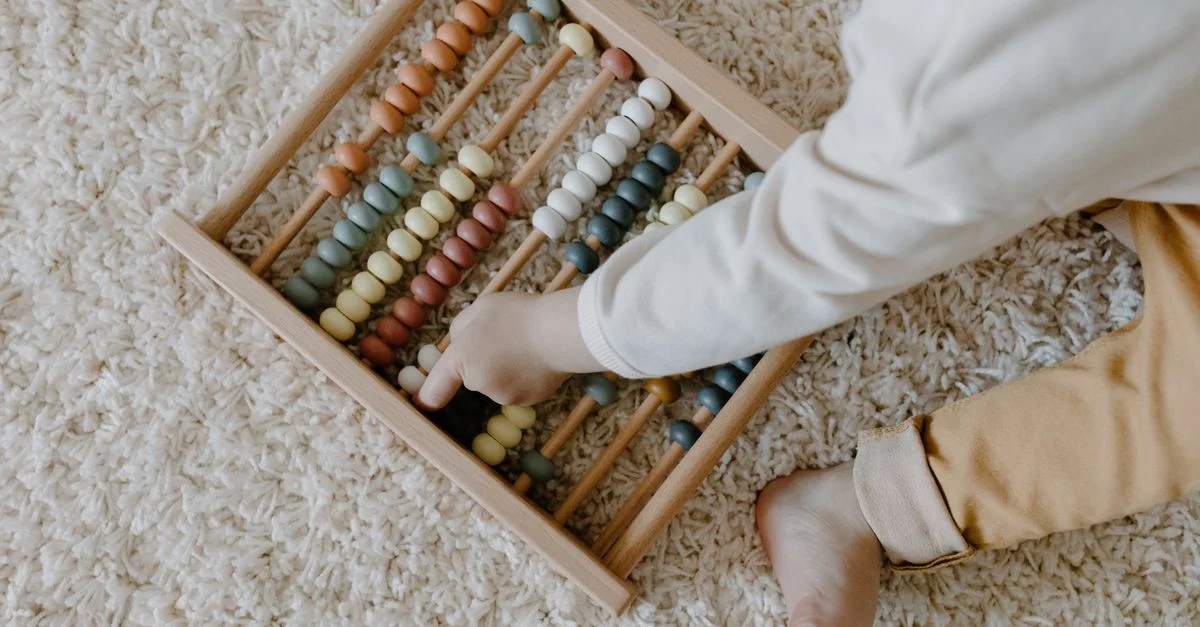 Un jeune enfant interagit avec un boulier en bois coloré, explorant l'apprentissage par le jeu.