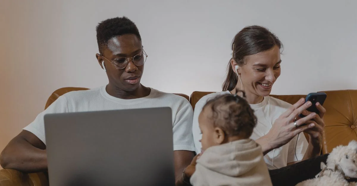 Una familia disfrutando de tiempo de calidad juntos utilizando dispositivos tecnológicos como laptops y smartphones.