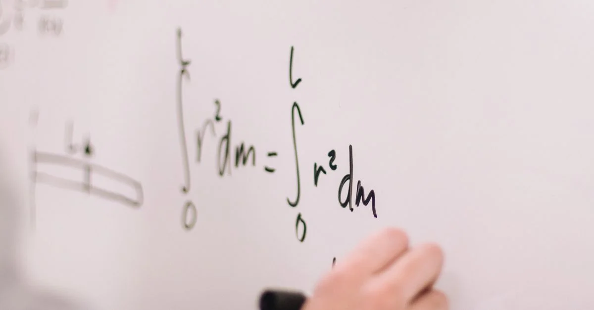 Persona escribiendo ecuaciones matemáticas en una pizarra blanca, enfocándose en integrales y fórmulas.