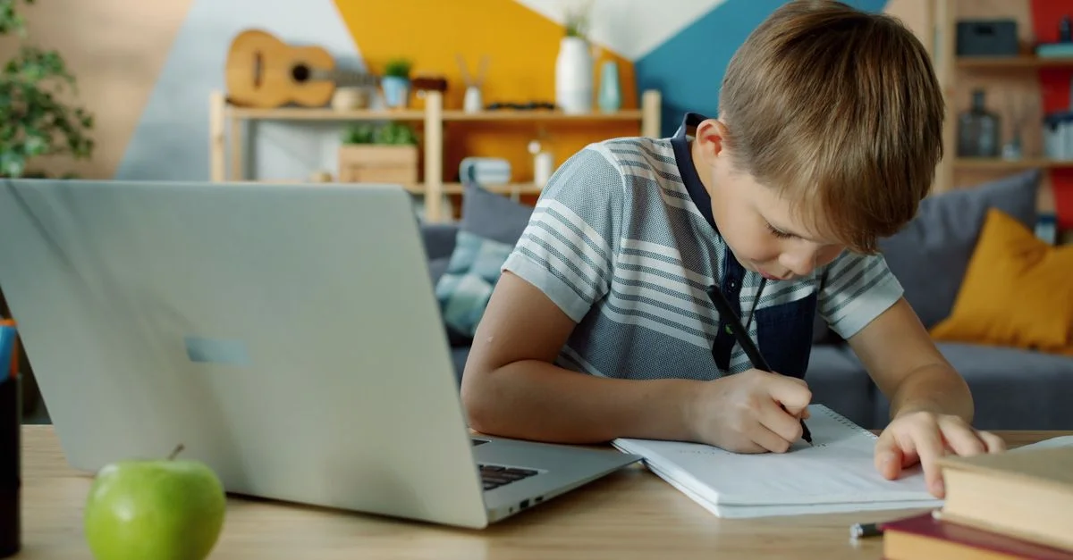 Un niño pequeño toma apuntes en casa usando una computadora portátil para aprender.